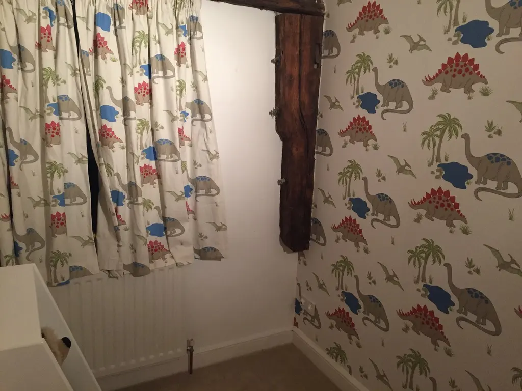 Empty small bedroom with dinosaur wallpaper, a timber beam and a radiator