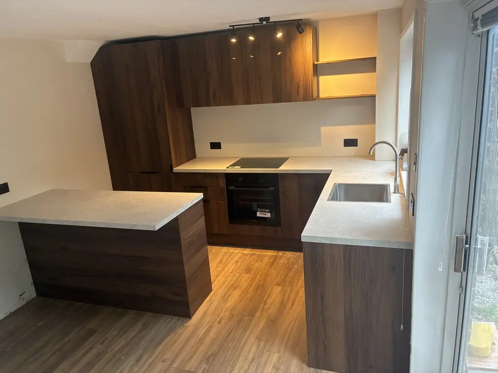 Walnut-effect handleless kitchen with stone-effect worktops and peninsula