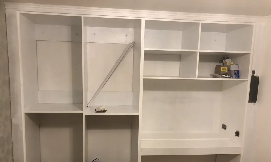 White primed built-in carcass with shelving and a desk shelf, before doors
